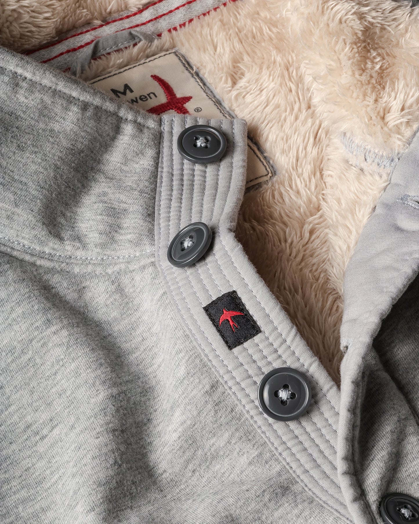 Close-up of a gray fleece with buttons and a brand label on a textured background