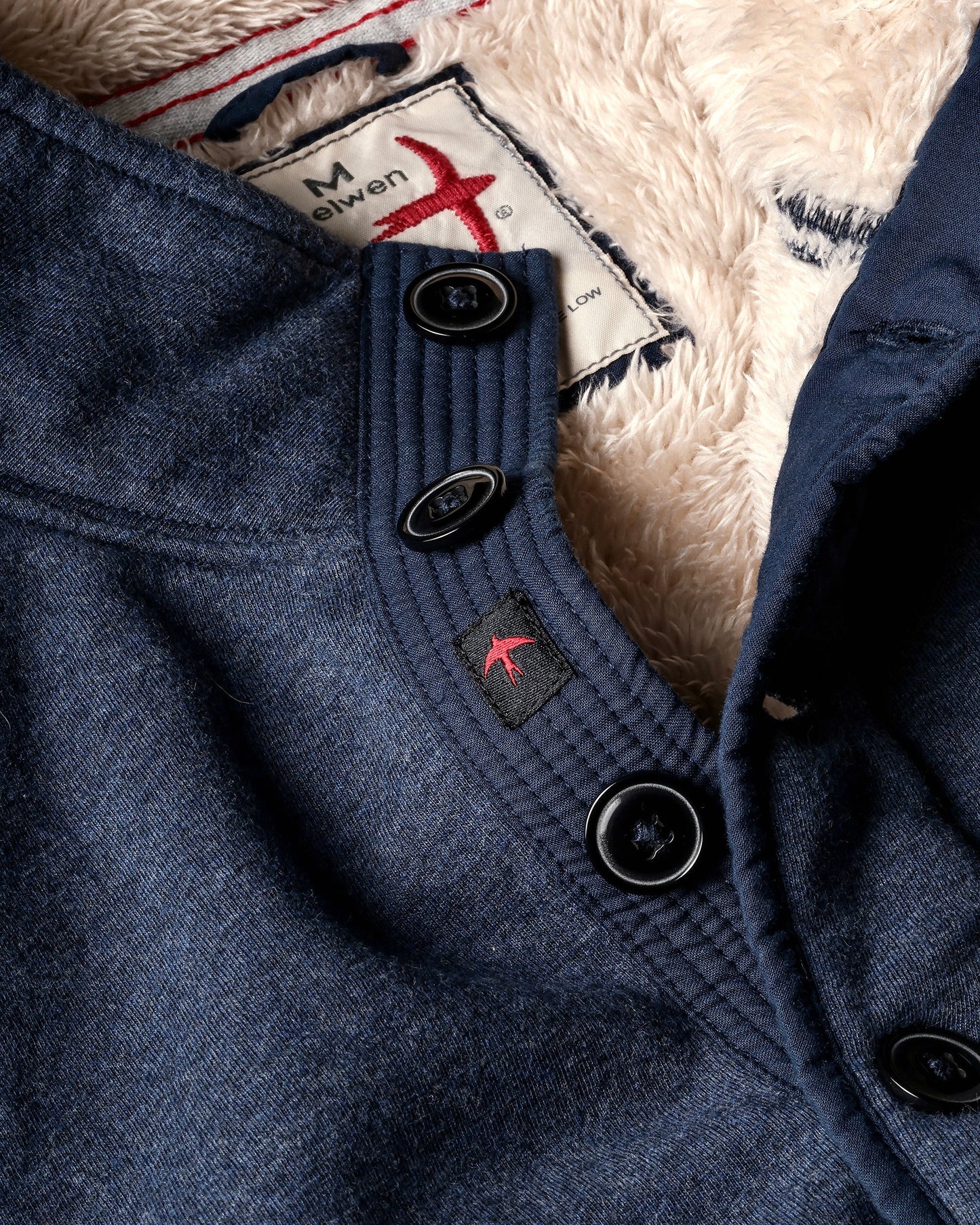 Close-up of a blue coat with buttons and a brand label on a textured background