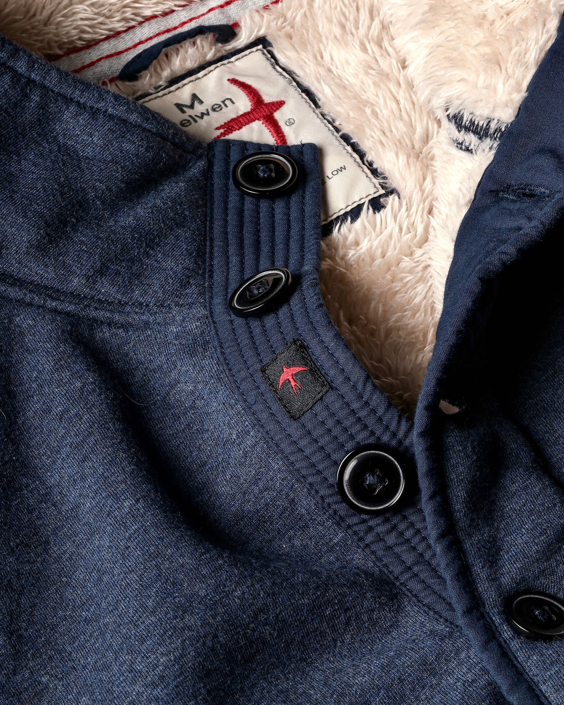 Close-up of a blue coat with buttons and a brand label on a textured background